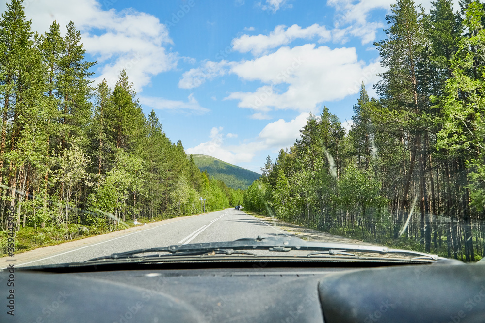 View from car window on the road and landscape with forest, tees, and blue sky with clouds. Landscape through windscreen with a relief