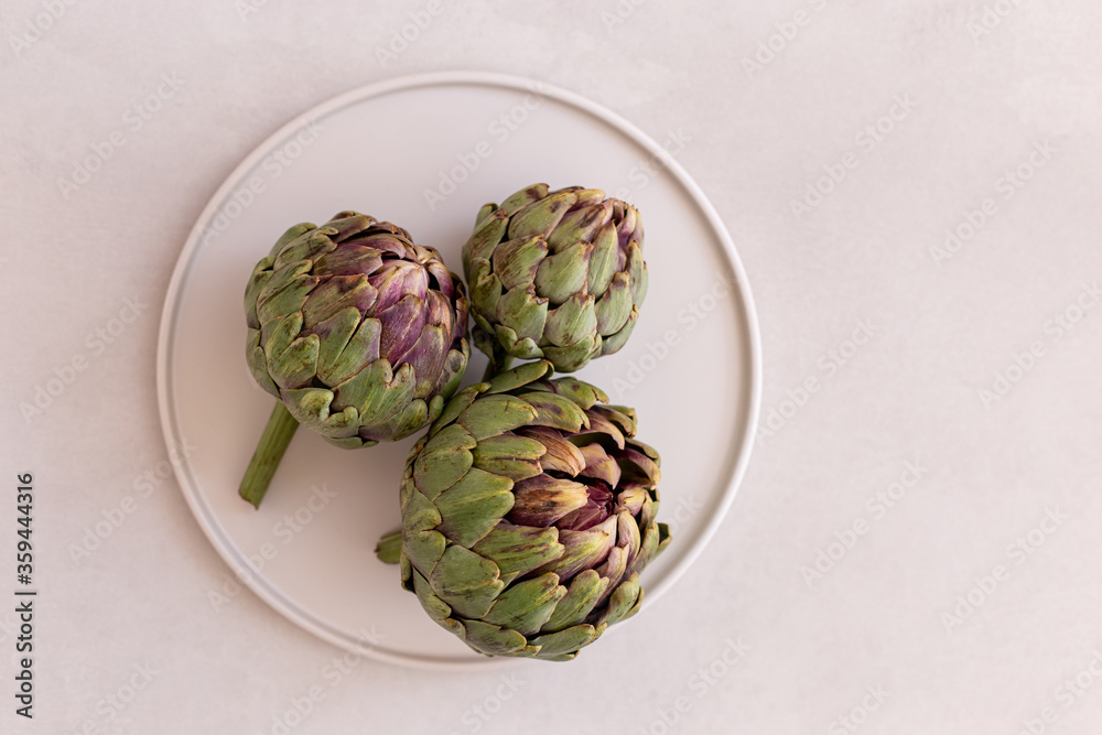 Obraz premium Minimalistic image ofartichokes in a white plate on a light gray