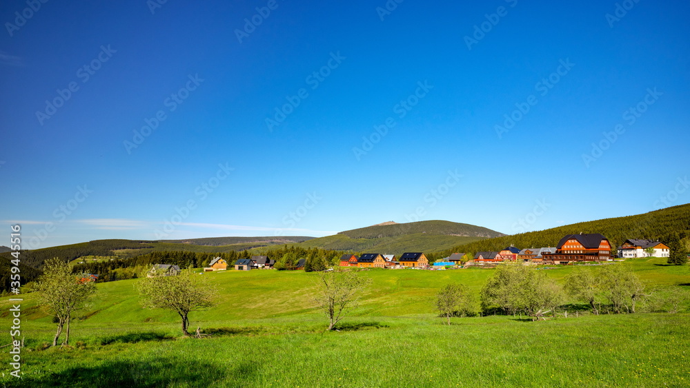 Small village of mountain huts in a green colorful hilly landscape with Snezka mountain in the background, Pomezni Boudy, Krkonose mountains, Czech Republic, Poland