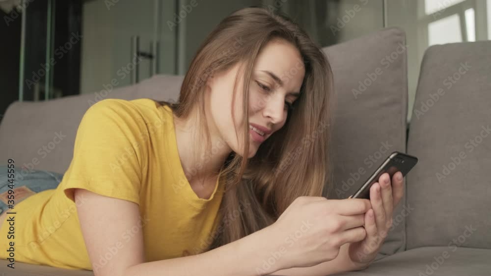 An attractive young woman is typing message on her smartphone while lying on the sofa at home An attractive young woman is typing message on her smartphone while lying on the sofa at home