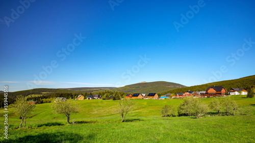 Small village of mountain huts in a green colorful hilly landscape with Snezka mountain in the background, Pomezni Boudy, Krkonose mountains, Czech Republic, Poland photo