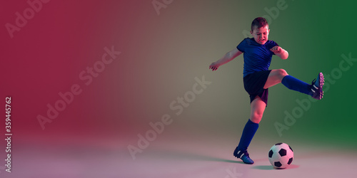 Flyer with copyspace. Teen male football player on gradient background in neon light. Caucasian boy training, practicing on the run, in jump. Concept of sport, competition, winning, motion, action. © master1305