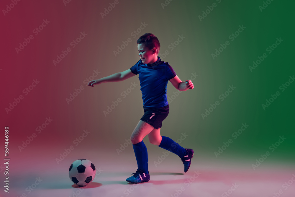 Winner. Teen male football or soccer player on gradient background in neon light. Caucasian boy training, practicing on the run, in jump. Concept of sport, competition, winning, motion, action.