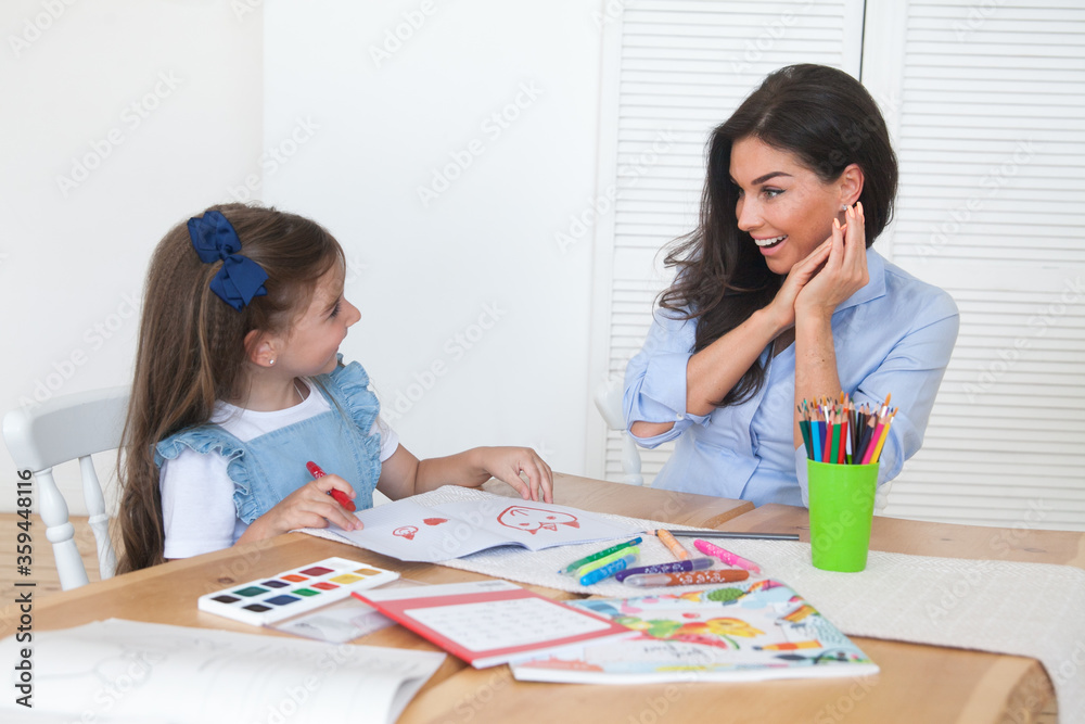 Smiling mother and daughter preparing for lessons and draws at the table with pencils and paints. Parent and pupil of preschool. First day of fall autumn. Girl from elementary class, back to school Smiling mother and daughter preparing for lessons and draws at the table with pencils and paints. Parent and pupil of preschool. First day of fall autumn. Girl from elementary class, back to school
