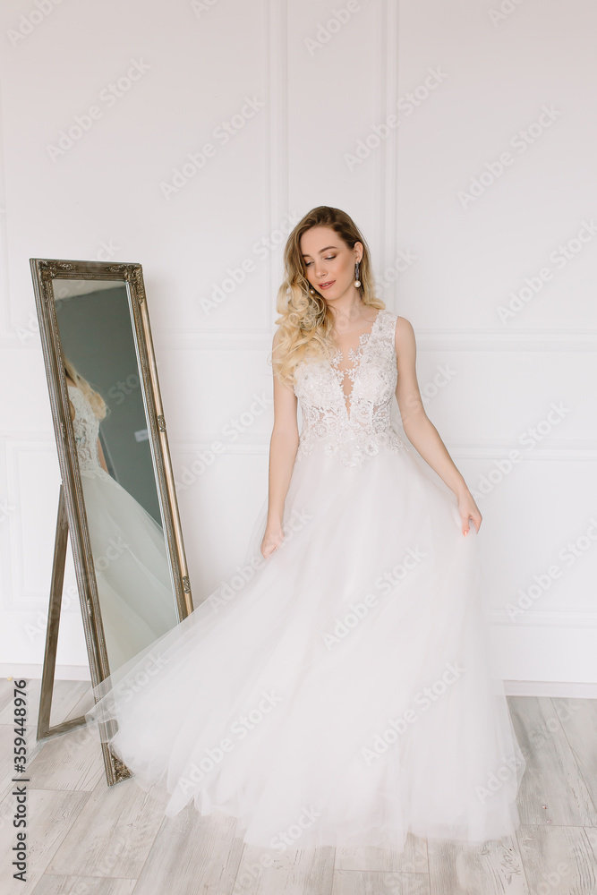 Beautiful girl woman bride in a delightful wedding dress with a bouquet of flowers dancing in front of a mirror portrait of a blonde with blue eyes holding Beautiful girl woman bride in a delightful wedding dress with a bouquet of flowers dancing in front of a mirror portrait of a blonde with blue eyes holding
