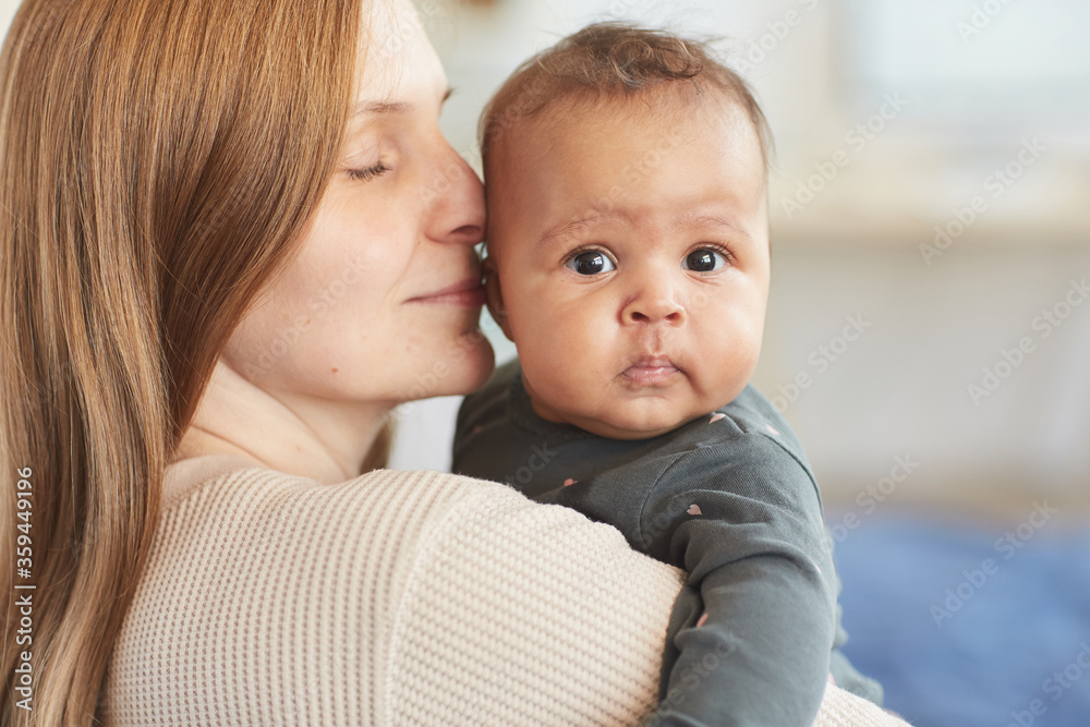 Close up portrait of mature Caucasian mother holding cute mixed-race baby looking at camera, copy space Close up portrait of mature Caucasian mother holding cute mixed-race baby looking at camera, copy space