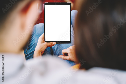 Cropped back view of couple in love watching video online on touch pad with blank screen area for internet advertisement using wireless 4G connection.Selective focus on digital tablet with copy space