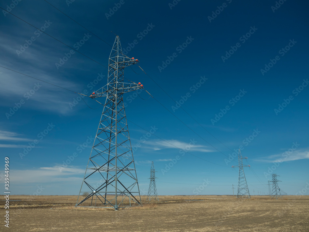 Front view of a line of metal poles of a high voltage power line with red plastic circles at the top.
