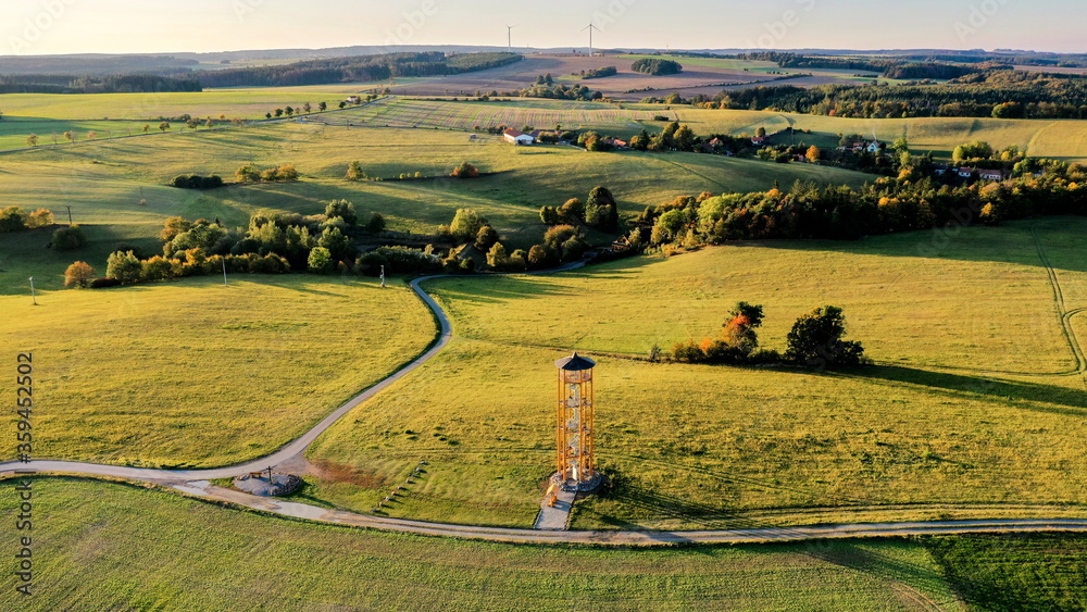 Obraz premium Landscape with fields during sunset and yellow metal lookout tower in the foreground, aerial photo, Czech Republic