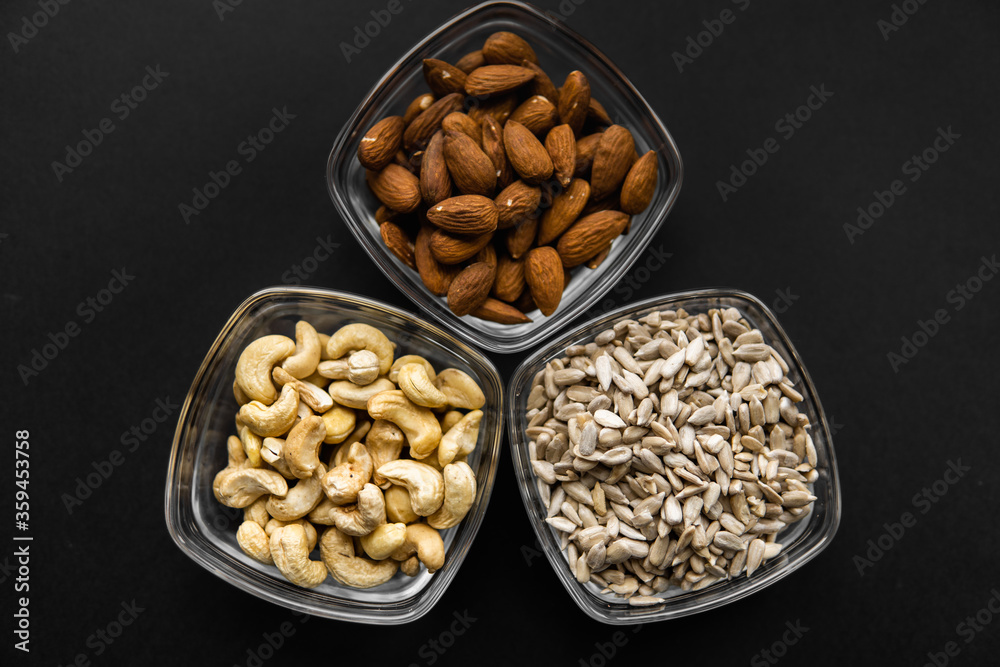 Almond, cashew and sunflower seeds in a small plates which standing on a black table. Nuts is a healthy vegetarian protein and nutritious food. Almond, cashew and sunflower seeds in a small plates which standing on a black table. Nuts is a healthy vegetarian protein and nutritious food.