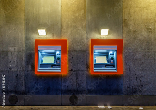 Two orange lined ATM machines on a concrete wall at night, with no people in sight