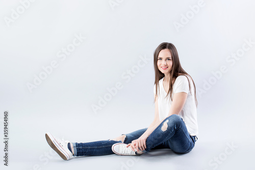 Woman in jeans and white t-shirt with long hair sits on the floor in studio.