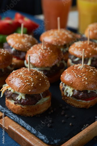 Juicy burgers with onion rings, cucumbers, lettuce, cheese on a black stone background