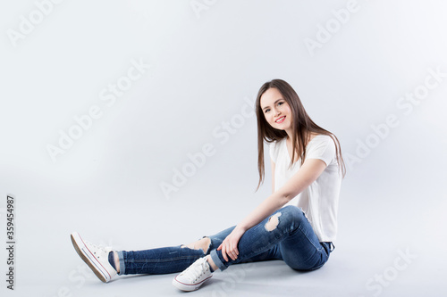 Beautiful woman in a white t-shirt and jeans sits on the floor in studio.