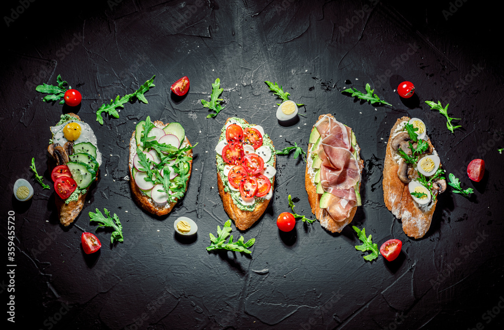 Traditional italian bruschetta on toasted slices of baguette seasoned with spice and herbs and garnished with fresh basil on a dark background