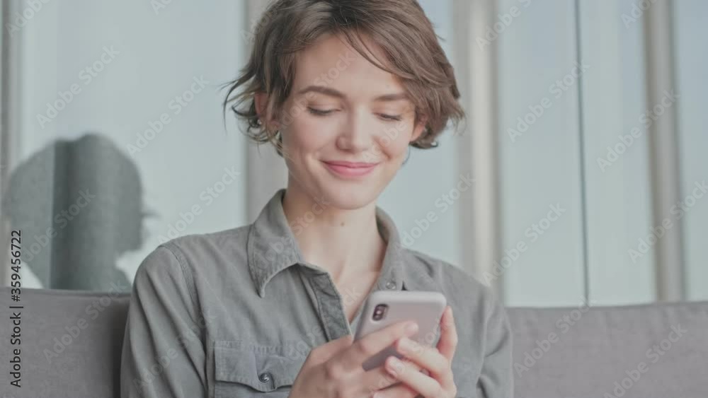 Happy young pretty woman using smartphone while sitting on sofa at home Happy young pretty woman using smartphone while sitting on sofa at home