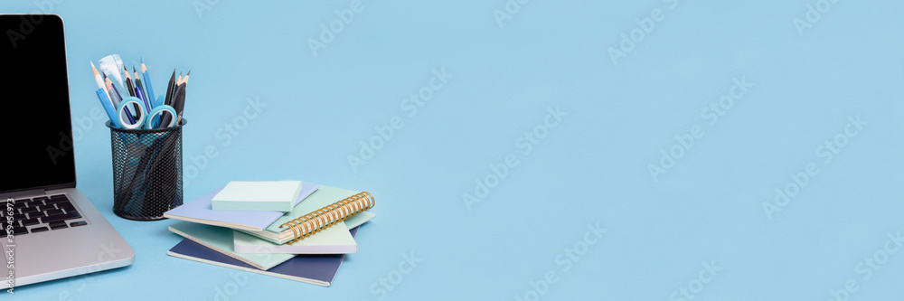 Laptop, stack of notepads, stand with stationery on a blue background.  Banner with workspace concept. Stock Photo | Adobe Stock