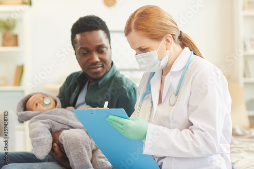 Side view portrait of female doctor writing on clipboard during home visit for baby checkup, copy space