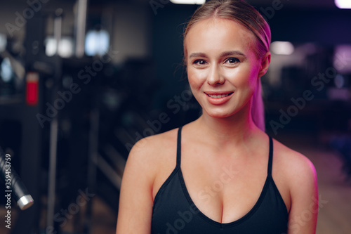 Close up portrait of a young blonde woman in sport bra in a dark gym