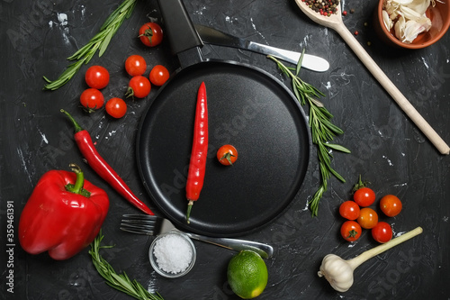 round frying pan, fresh rosemary,fresh cherry tomatoes, fresh chilli peppers, garlic, lime and sea salt on black background.Top view