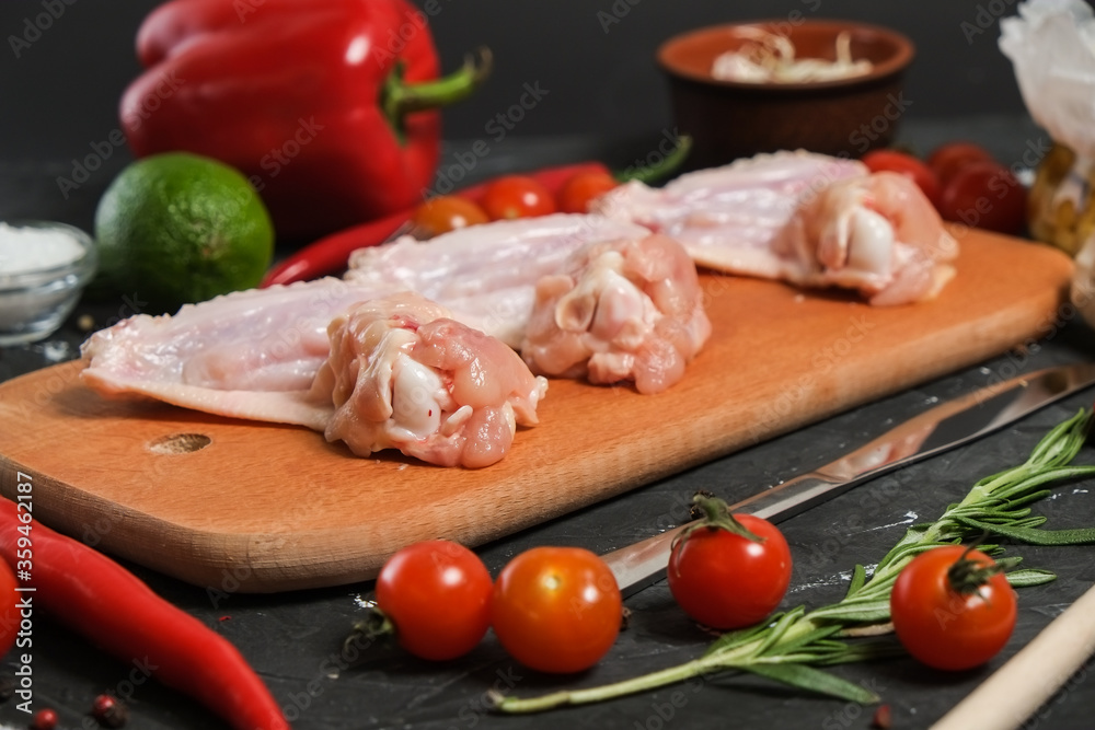 Chicken wings in a wooden Cutting board, fresh rosemary, fresh cherry tomatoes, fresh chili peppers, garlic, lime and sea salt on a black background. Chicken wings in a wooden Cutting board, fresh rosemary, fresh cherry tomatoes, fresh chili peppers, garlic, lime and sea salt on a black background.