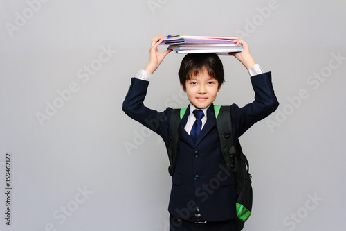 Close-up portrait of an Asian schoolboy holding his textbooks on his head and smiling