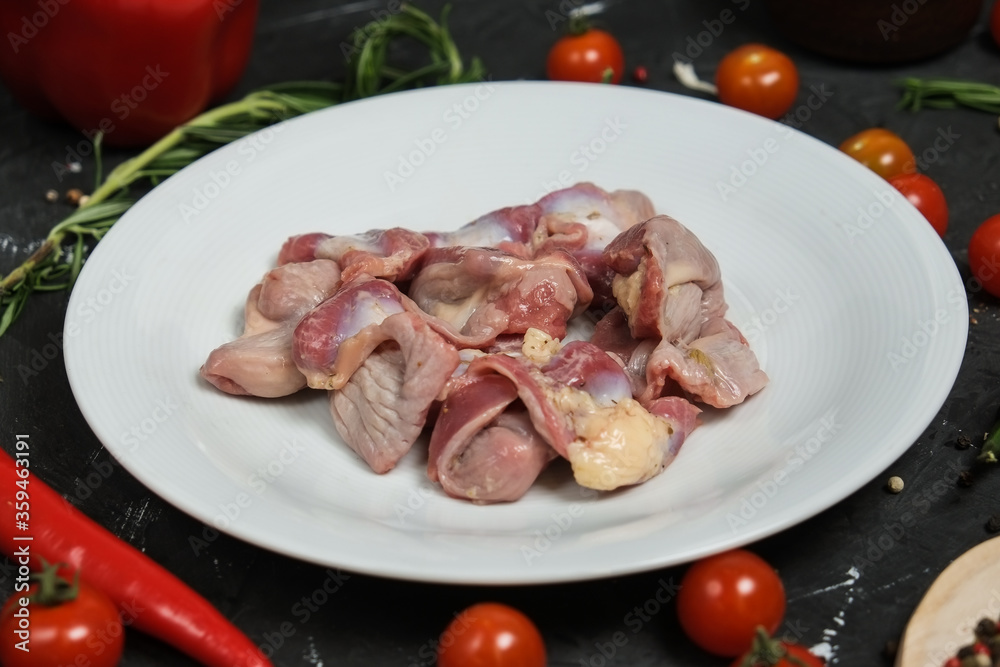 Chicken ventricles in a in a white plate, fresh rosemary, fresh cherry tomatoes, fresh chili peppers, garlic, lime and sea salt on a black background. Chicken ventricles in a in a white plate, fresh rosemary, fresh cherry tomatoes, fresh chili peppers, garlic, lime and sea salt on a black background.