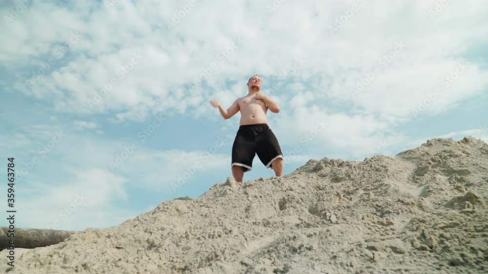 Funny Fat Man with Long Hair Stands on a Pile of Sand and Beats Himself in the Chest Funny Fat Man with Long Hair Stands on a Pile of Sand and Beats Himself in the Chest