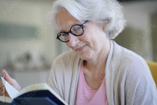 Senior woman relaxing in armchair and reading book