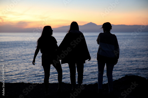 silhouette of three girls, three young women, at sunset looking at the horizon. Beautiful background. Local travel context, friends' summer trip