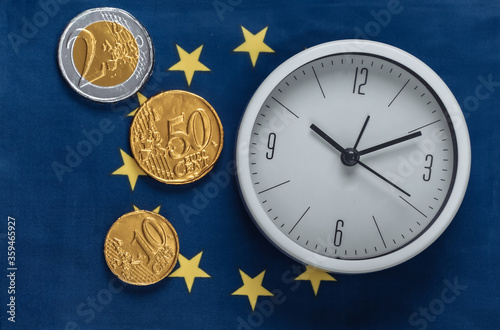 White clock with coins on the background of the Euro Union flag photo