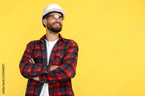 Handsome bearded engineer or constructor man in plai shirt standing over yellow background. Looking away. photo