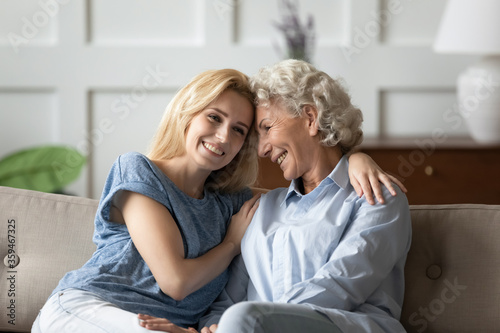 Grown up granddaughter spend time with old grandmother, adult daughter sitting on couch with aged mother two women embracing smiling enjoy pleasant chat warm relations, express caress and love concept