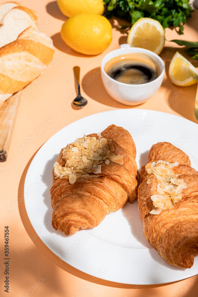 croissants, baguette, lemons and cup of coffee for breakfast on beige table