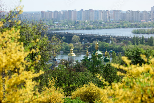 View to Kyiv city from botanical garden. Beautiful spring view of Vydubychi monastery and Dnipro river with blooming trees in botanical garden. Picturesque spring scene. photo