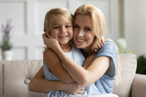 Head shot portrait beautiful mother cuddles lovely little daughter family sitting on sofa smile look at camera spend time together enjoy games playing having fun relish funny activity at home concept