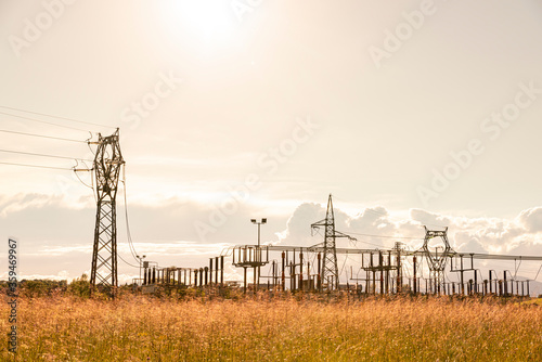 Electrical pylon and converter station at sunset, among cultivated fields.