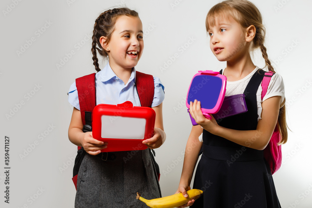 Pupils of primary school with lunch-boxes in hands. Girls with backpacks are eating fruit. Beginning of lessons. First day of fall. Pupils of primary school with lunch-boxes in hands. Girls with backpacks are eating fruit. Beginning of lessons. First day of fall.