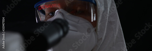 Close-up of man in protective costume suit with coronavirus sign on glasses. White antibacterial clothes. Worker in respirator. Health virus epidemic and covid19 concept