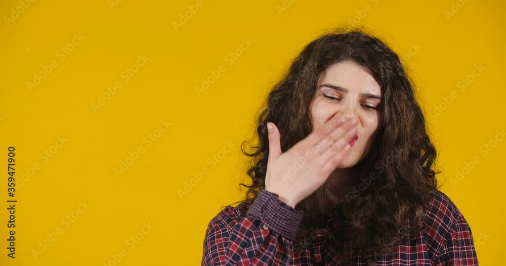 Close-up attractive plus-size model posing. A curly-haired brunette on a bright yellow studio background demonstrating different emotions. Girl Blowing sweet air kiss with her hand Close-up attractive plus-size model posing. A curly-haired brunette on a bright yellow studio background demonstrating different emotions. Girl Blowing sweet air kiss with her hand