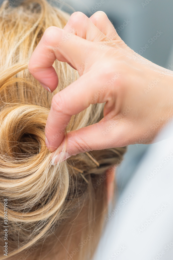 Obraz premium Close up rear view of hairdresser making hairstyle for long hair of blonde woman.