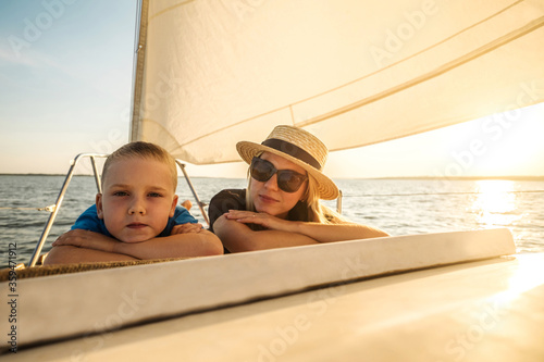 Happy traveler mother and son enjoying sunset from deck of sailing boat moving in sea at evening time. Bonding Travel, Summer, Holidays, Journey, Trip, Lifestyle, Yachting concept.