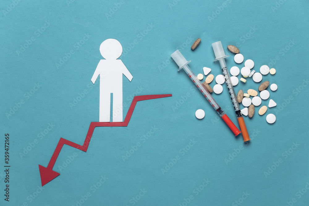 Syringes and pills, paper man descends along red curved arrow tending downward. Blue background. Symbol of social degradation, drug addiction Syringes and pills, paper man descends along red curved arrow tending downward. Blue background. Symbol of social degradation, drug addiction