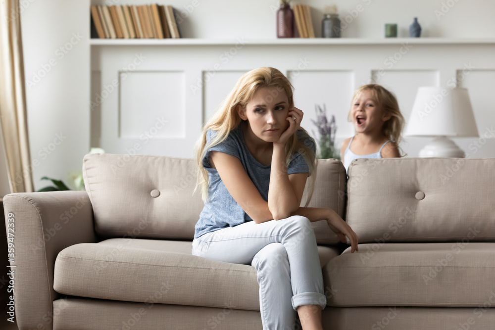 Screaming noisy little daughter brings mom to despair, parent feels tired resting seated on couch in living room. Hyperactive and naughty disobedient child, omission in upbringing or nurture concept Screaming noisy little daughter brings mom to despair, parent feels tired resting seated on couch in living room. Hyperactive and naughty disobedient child, omission in upbringing or nurture concept