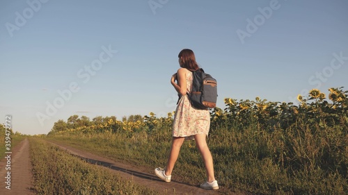 farmer's daughter inspects father's field. Girl walk on field with sunflowers at sunset. young girl travels through countryside with backpack, she walks along field of blooming sunflower.