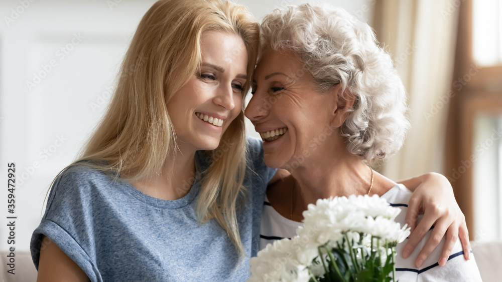 Close up beautiful grown up daughter hug elderly mom congratulates her with 8-march spring holiday make surprise gave white chrysanthemum flowers. Mother Day, birthday, life event celebration concept