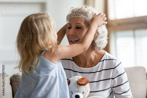 Cuadro en lienzo Cutie small granddaughter imagines herself like princess play with elderly grandmother puts on her head crown appointing her a queen