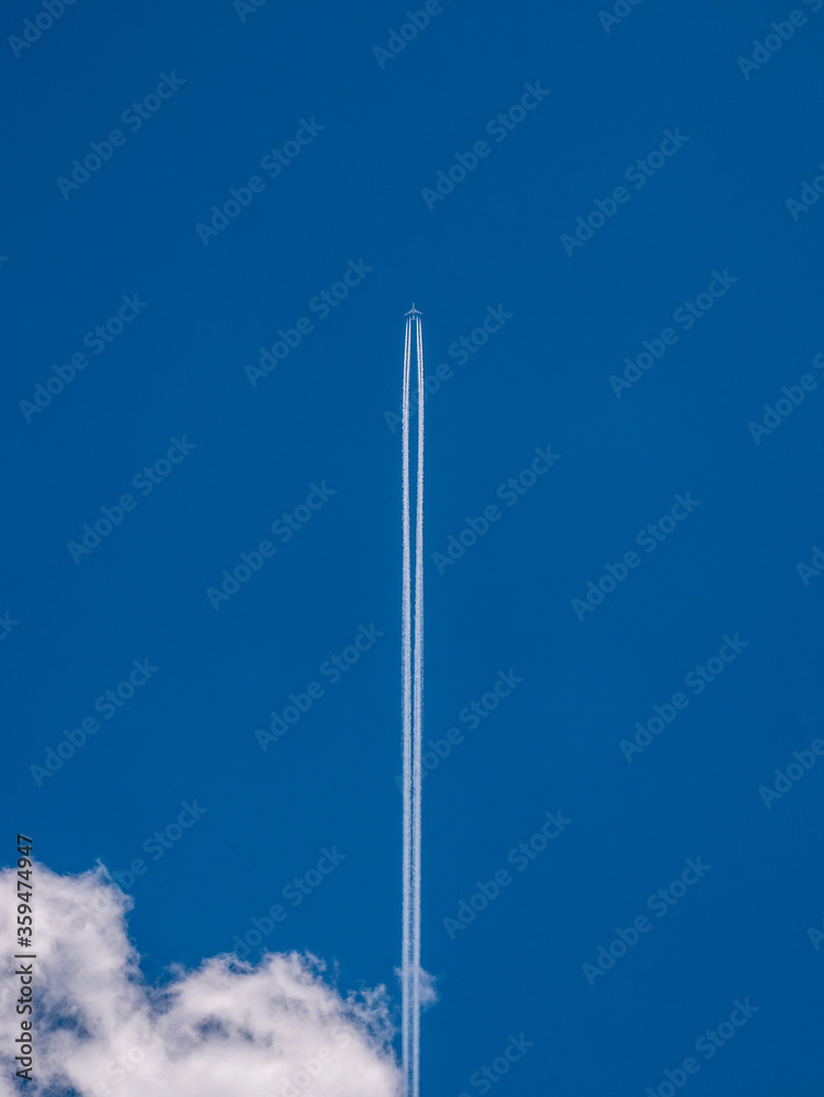 Airplane in the blue sky with a condensation trail and a cloud in the lower left corner Airplane in the blue sky with a condensation trail and a cloud in the lower left corner