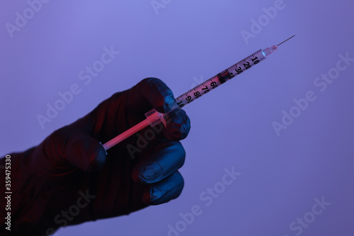 Fototapeta Naklejka Na Ścianę i Meble -  A gloved hand holds a syringe. Red-blue neon light.