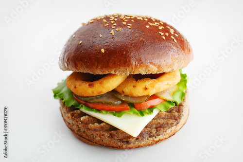 Juicy burger from dark flour with onion rings, cucumbers, lettuce, cheese on a white background